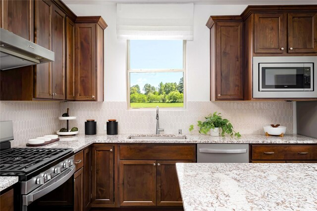 kitchen featuring backsplash, appliances with stainless steel finishes, light stone countertops, a sink, and extractor fan