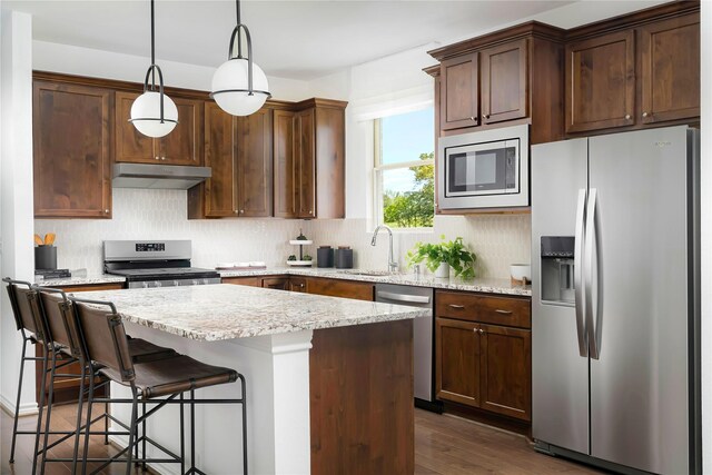 kitchen featuring a kitchen island, stainless steel appliances, decorative backsplash, under cabinet range hood, and pendant lighting