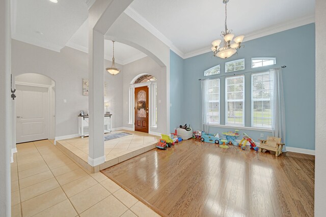 tiled foyer with crown molding, arched walkways, baseboards, and a notable chandelier