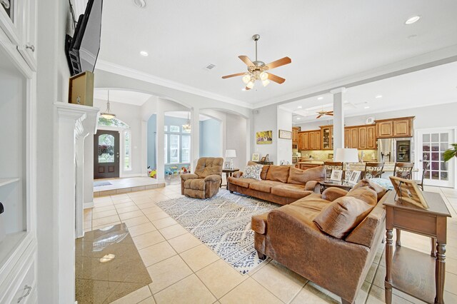 living area with ceiling fan, visible vents, crown molding, arched walkways, and light tile patterned floors