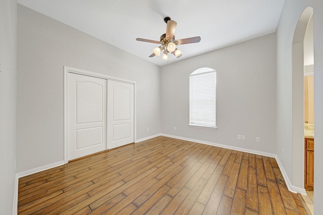 unfurnished bedroom with arched walkways, baseboards, wood-type flooring, and a closet
