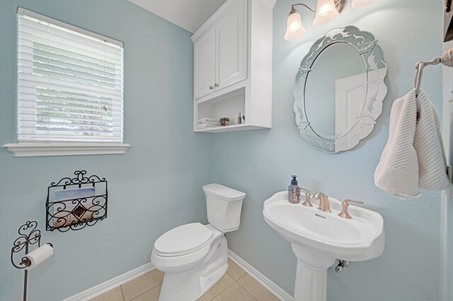 half bath featuring baseboards, tile patterned flooring, and toilet