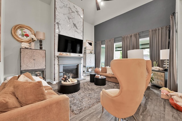 living area with high vaulted ceiling, ceiling fan, a large fireplace, and wood finished floors