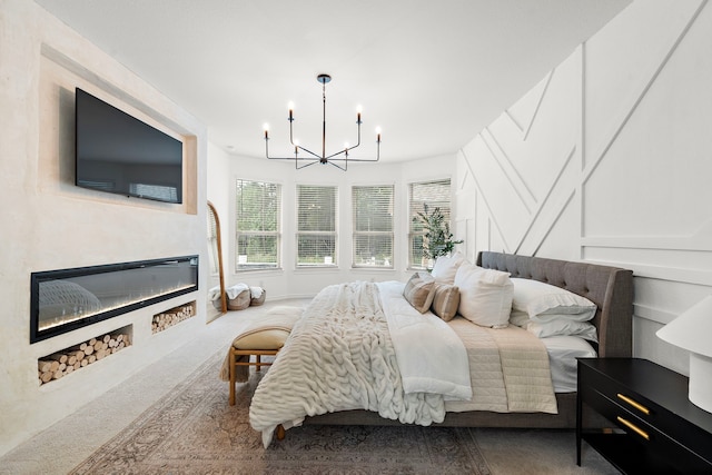 carpeted bedroom with an inviting chandelier, a decorative wall, and a glass covered fireplace