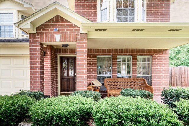 doorway to property featuring covered porch, brick siding, fence, and visible vents