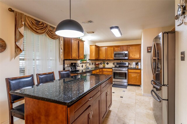 kitchen featuring visible vents, brown cabinets, dark stone countertops, appliances with stainless steel finishes, and decorative light fixtures