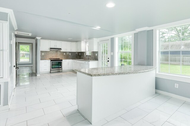 kitchen featuring appliances with stainless steel finishes, tasteful backsplash, light stone countertops, white cabinets, and under cabinet range hood
