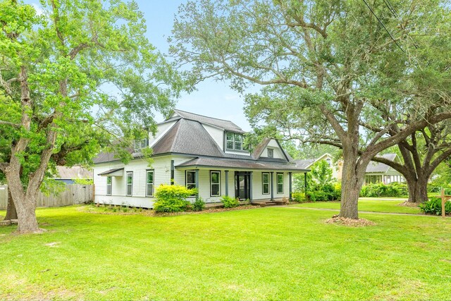 view of front of house with fence, roof with shingles, covered porch, and a front lawn