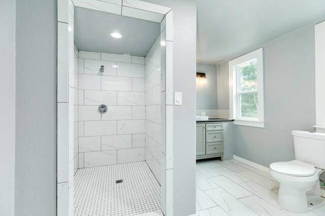 full bath with a tile shower, vanity, toilet, marble finish floor, and baseboards