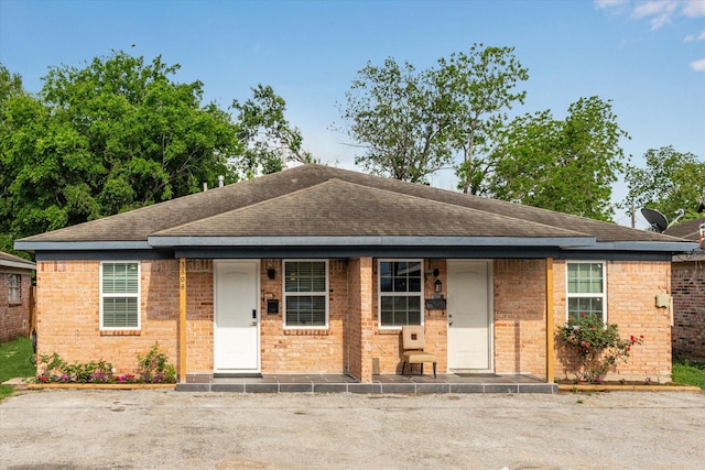 view of front of home featuring brick siding, roof with shingles, and a porch
