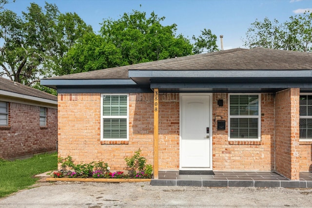 view of front of house featuring brick siding and roof with shingles