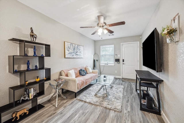 living area featuring baseboards, a textured wall, ceiling fan, and wood finished floors