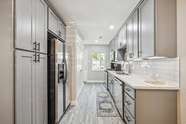 kitchen with light wood-type flooring, a sink, gray cabinets, and stainless steel appliances