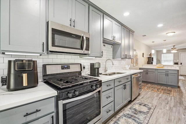 kitchen with a sink, gray cabinets, stainless steel appliances, light wood-type flooring, and backsplash