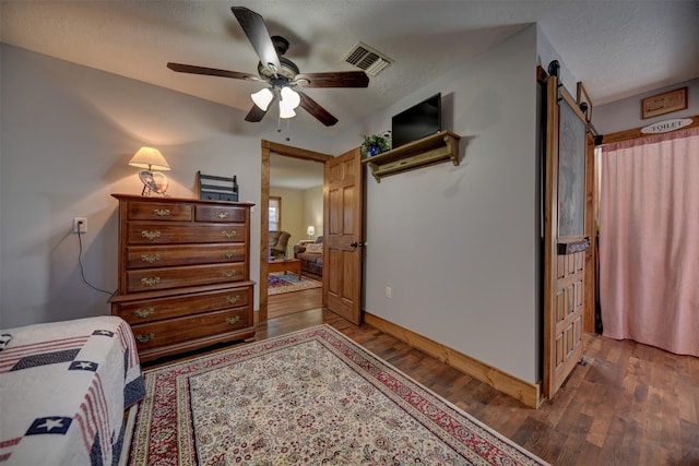 bedroom featuring a barn door, a ceiling fan, baseboards, wood finished floors, and visible vents