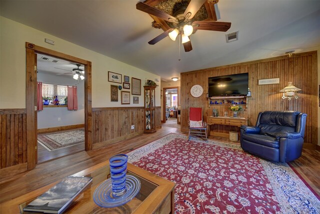 living area featuring wooden walls, ceiling fan, wood finished floors, and visible vents