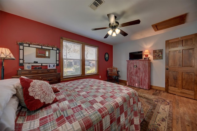 bedroom with ceiling fan, attic access, baseboards, wood finished floors, and visible vents