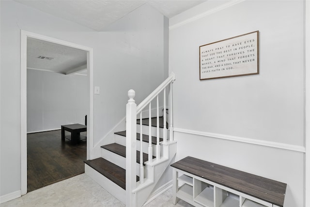 stairway with visible vents, ornamental molding, a textured ceiling, and baseboards