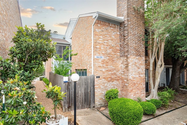 view of property exterior featuring brick siding, fence, and a chimney