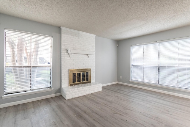 unfurnished living room with baseboards, a brick fireplace, a textured ceiling, and wood finished floors