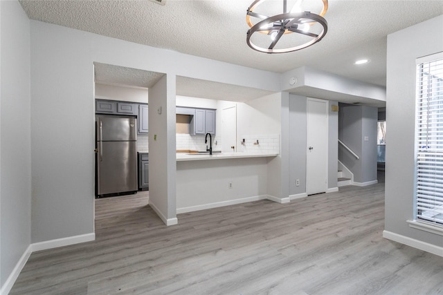interior space featuring a sink, light wood finished floors, light countertops, a textured ceiling, and freestanding refrigerator
