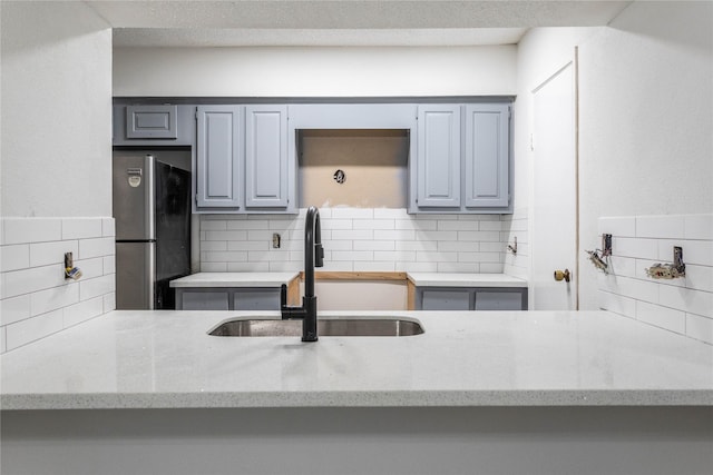 kitchen with freestanding refrigerator, gray cabinetry, decorative backsplash, and a sink