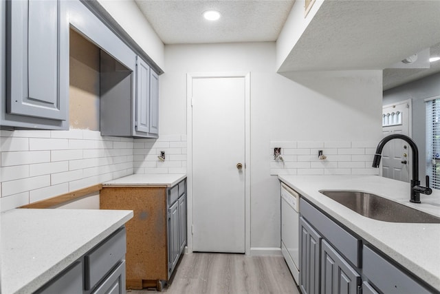 kitchen featuring light wood-style floors, gray cabinets, tasteful backsplash, a sink, and dishwasher