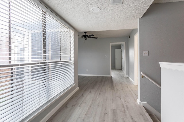 hallway featuring light wood-style floors, baseboards, a textured ceiling, and visible vents