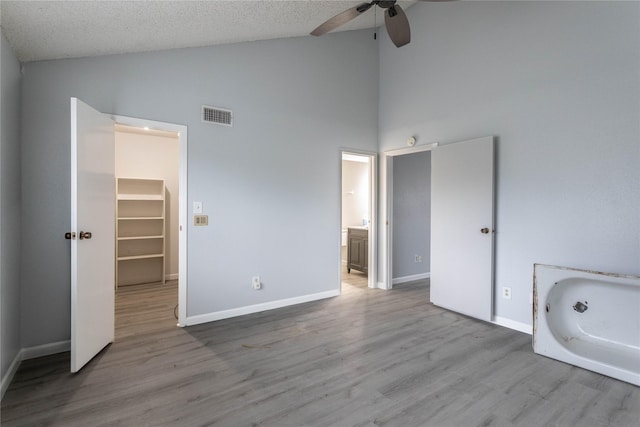 unfurnished bedroom with high vaulted ceiling, visible vents, wood finished floors, and a spacious closet