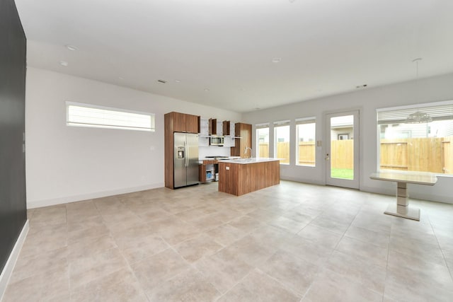 interior space featuring appliances with stainless steel finishes, brown cabinets, light countertops, baseboards, and an island with sink
