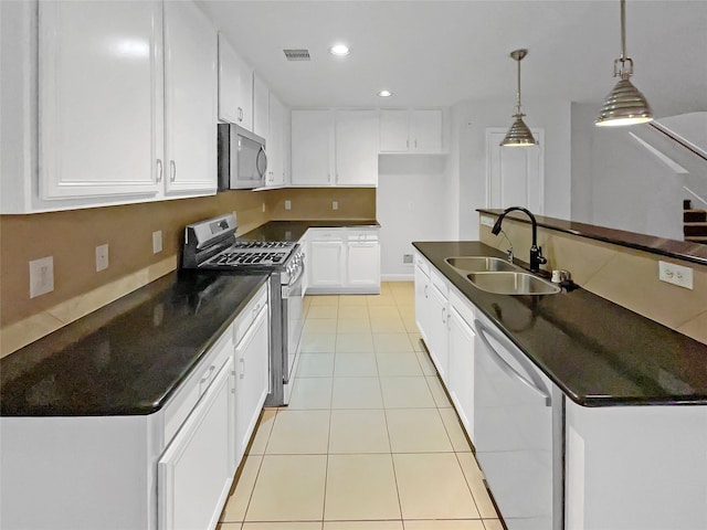 kitchen featuring dark countertops, a sink, light tile patterned floors, stainless steel appliances, and white cabinetry