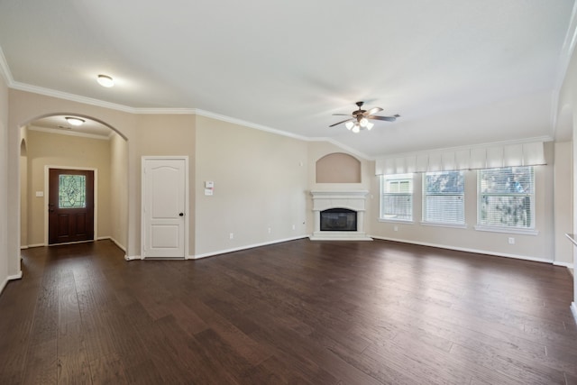 unfurnished living room with a ceiling fan, arched walkways, plenty of natural light, dark wood-style flooring, and crown molding