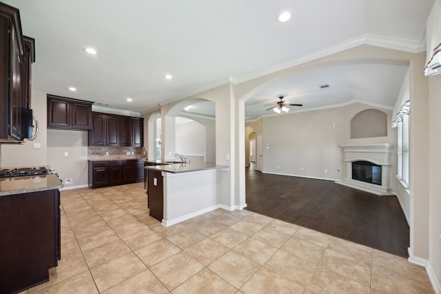 kitchen with ceiling fan, arched walkways, open floor plan, dark brown cabinets, and decorative backsplash