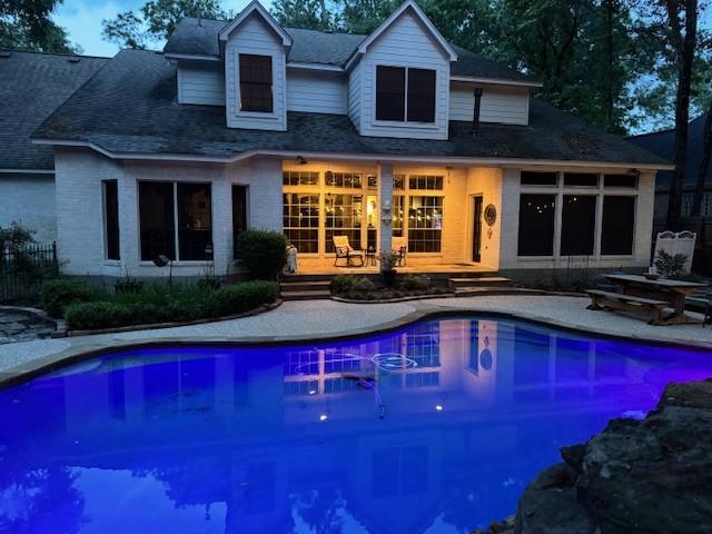 back of house with roof with shingles, a wooden deck, a patio area, and an outdoor pool
