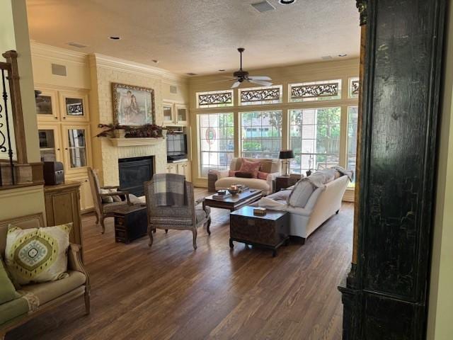 living area with visible vents, ornamental molding, a fireplace, a ceiling fan, and dark wood finished floors