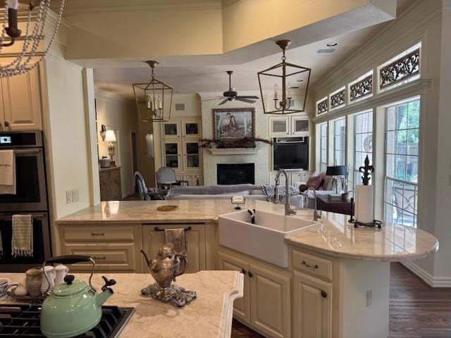 kitchen with stainless steel double oven, a fireplace, a sink, ceiling fan with notable chandelier, and open floor plan