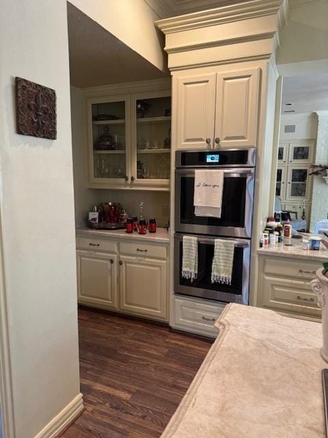 kitchen featuring crown molding, light countertops, double oven, glass insert cabinets, and dark wood-type flooring