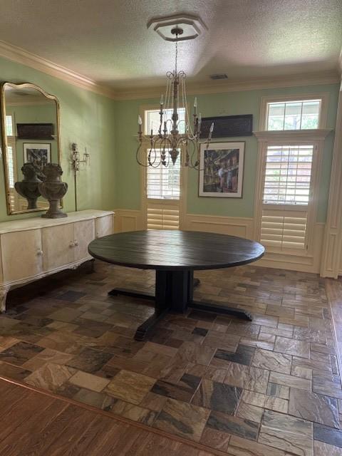 dining area featuring a textured ceiling, a chandelier, and wainscoting