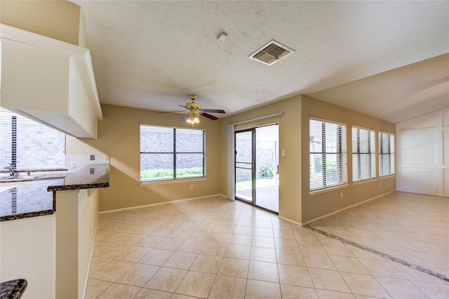 interior space with light tile patterned flooring, ceiling fan, a textured ceiling, baseboards, and visible vents