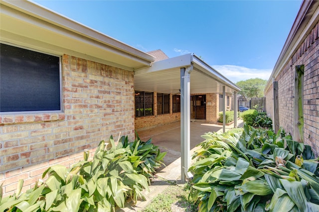 view of side of property featuring brick siding, a patio area, and fence
