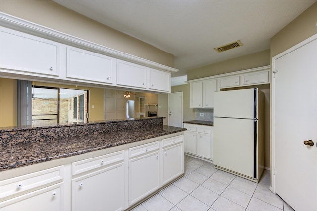 kitchen featuring white cabinets, freestanding refrigerator, dark stone counters, light tile patterned floors, and visible vents