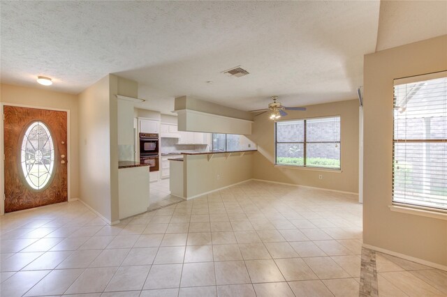 kitchen featuring dobule oven black, a ceiling fan, visible vents, white cabinets, and a peninsula