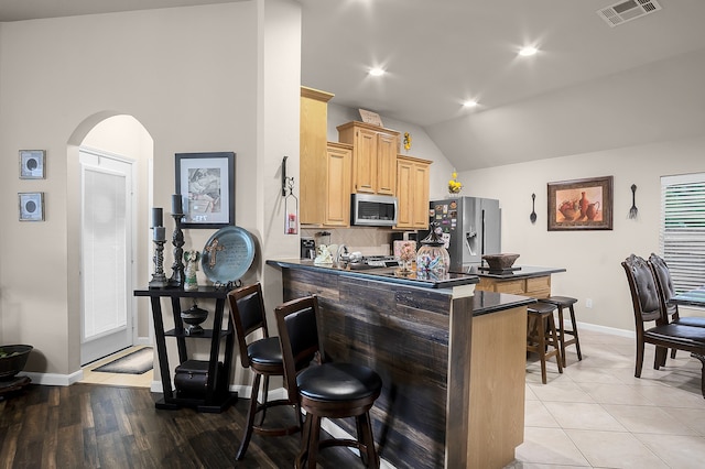 kitchen with light brown cabinetry, appliances with stainless steel finishes, visible vents, arched walkways, and vaulted ceiling