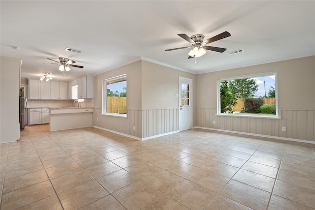unfurnished living room with ceiling fan, visible vents, ornamental molding, and light tile patterned floors