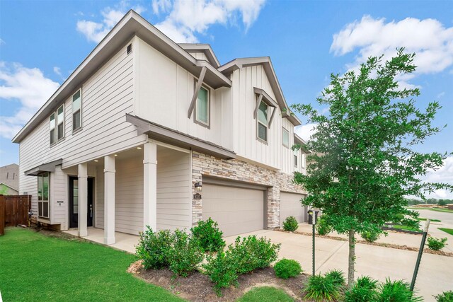 view of front of house featuring board and batten siding, driveway, a front lawn, an attached garage, and stone siding