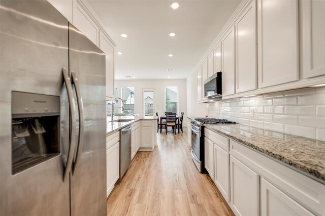 kitchen with a peninsula, light wood-type flooring, white cabinets, a sink, and appliances with stainless steel finishes