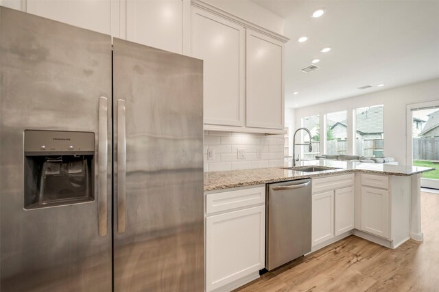 kitchen with a peninsula, light stone counters, a sink, light wood finished floors, and stainless steel appliances