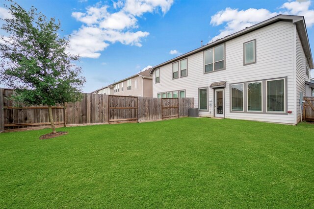 back of house featuring a fenced backyard, a yard, and central AC