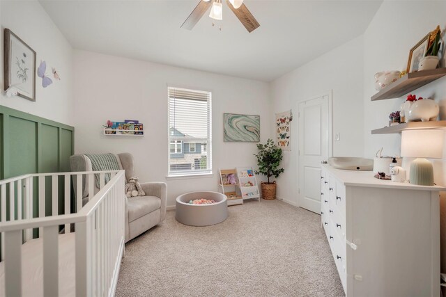 bedroom with a nursery area, baseboards, light carpet, and ceiling fan