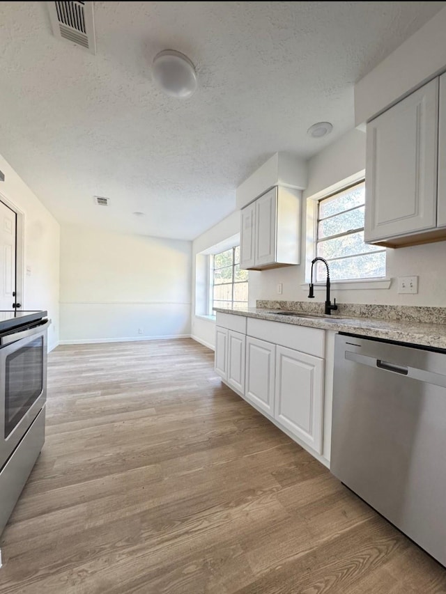 7810 Bunker Wood Ln, Houston, TX 77086 - kitchen with a sink, stainless steel appliances, a textured ceiling, light wood-style flooring, and white cabinetry